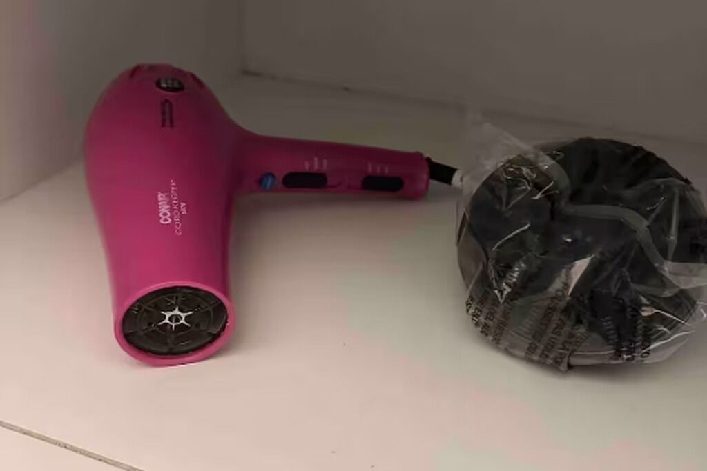 Un sèche-cheveux rose et un objet emballé dans du plastique, posés sur une surface blanche.