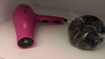 Un sèche-cheveux rose et un objet emballé dans du plastique, posés sur une surface blanche.