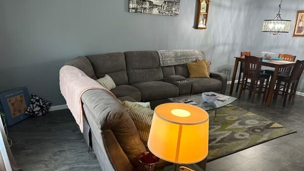 A living room with a sofa, a coffee table, a lamp, a dining table with chairs, and a patterned rug.