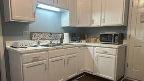 A kitchen with white cabinets, a microwave, a sink, and a breakfast sign.