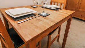 A wooden dining table set with plates, cutlery, and wine glasses, with a window and wooden cabinet in the background. - Riber (Matlock)