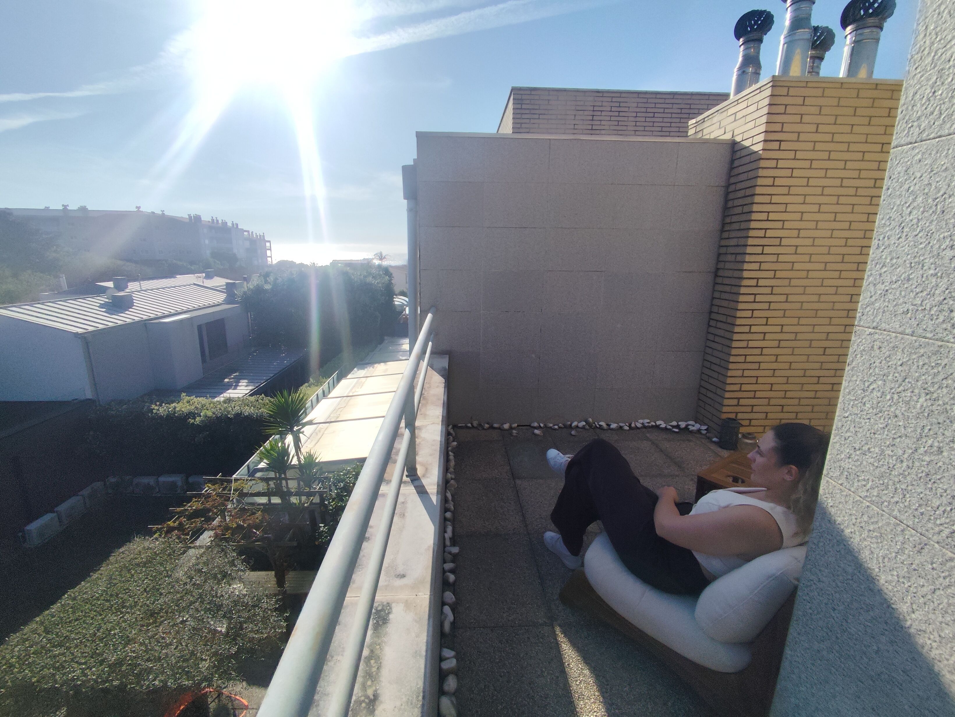 Uma pessoa sentada em varanda com vista para edifícios e céu claro.
