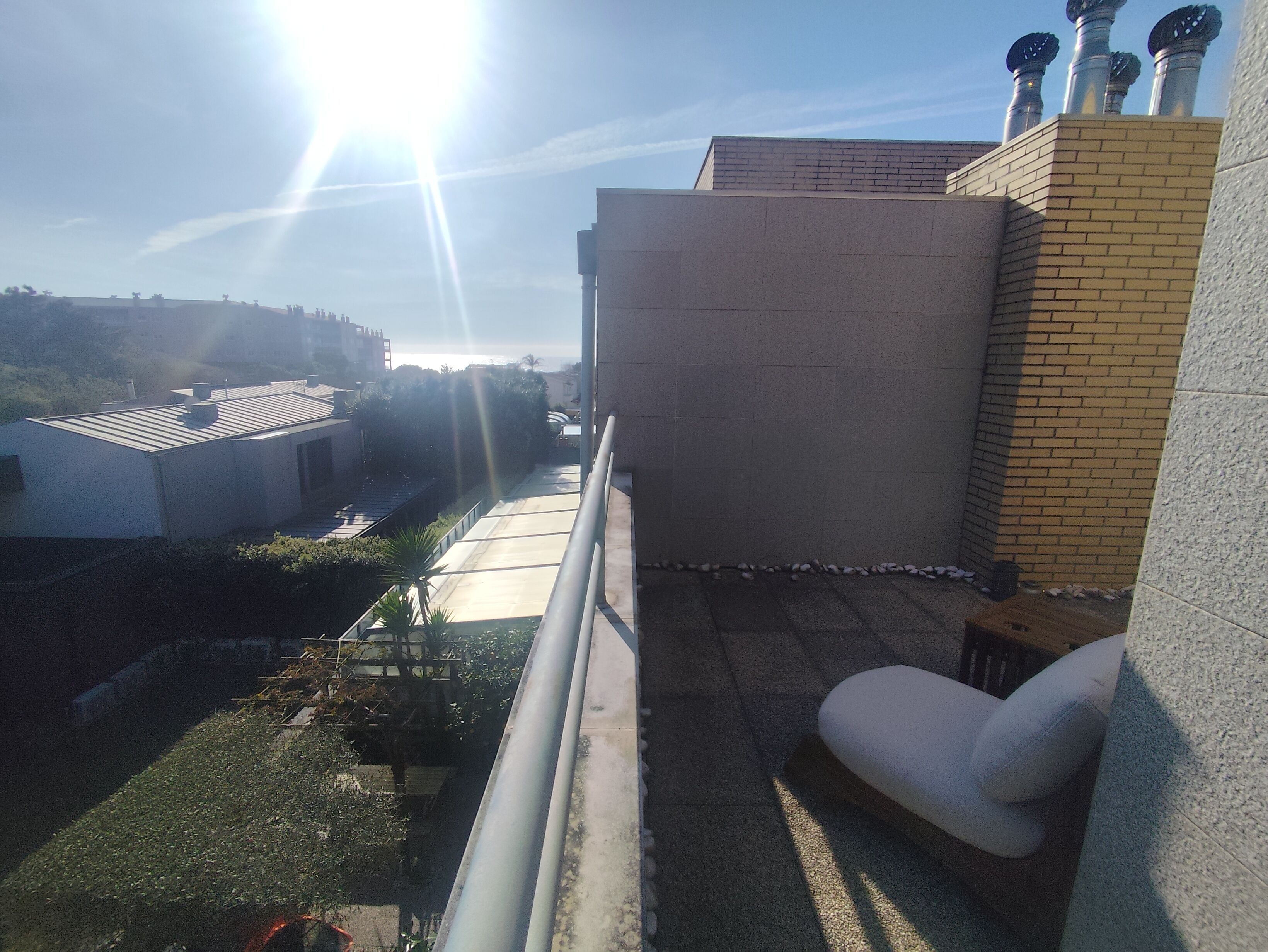 A balcony with a view of a residential area, a white chair, and a metal railing.
