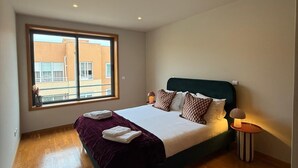 Une chambre avec une grande fenêtre, un lit avec des oreillers, une lampe de chevet et un plancher en bois.
