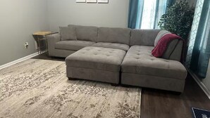 A sectional sofa in a living room with a patterned rug, a small side table, and a plant by the window. - Relax. Breathe. Enjoy. (Berea)