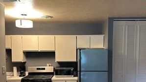 Una cocina compacta con estufa, microondas, refrigerador y gabinetes blancos.