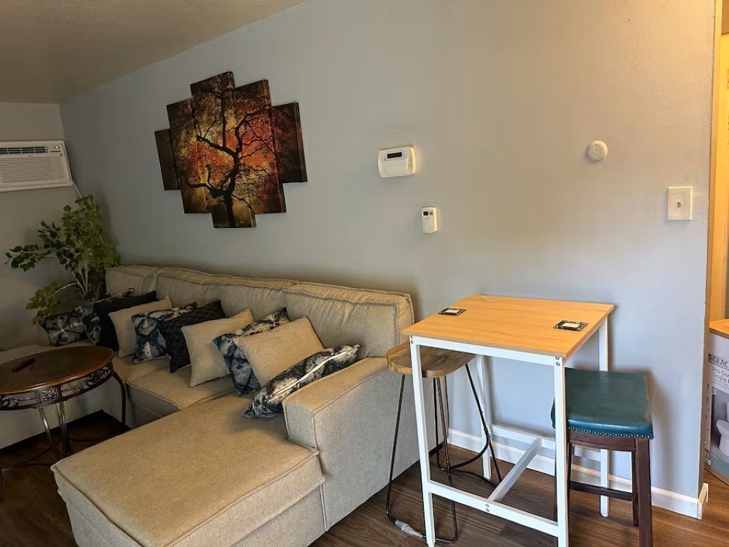 Una sala de estar con un sofá, una mesita, una obra de arte colgada en la pared y un termostato también instalado en la pared.