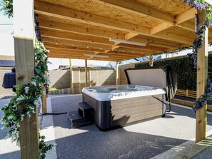 A hot tub under a wooden pergola with a view of a fenced area and a building in the background. - 1 Talbot Drive (Holywell)