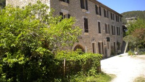 A stone building with multiple windows and a paved path leading to it. - Appartement de 76m2 dans maison historique (Fontaine-de-Vaucluse)