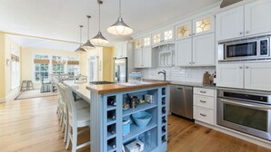 A modern kitchen with white cabinets, a central island with blue shelves, stainless steel appliances, and pendant lighting. - Large, 4,300 sq. ft. custom built 5 BR home on private 2.2 acres in Watch Hill (Westerly)