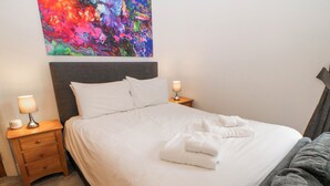 A neatly made bed with white linens, two bedside tables with lamps, and a colorful abstract painting on the wall. - Arkwright (Matlock)