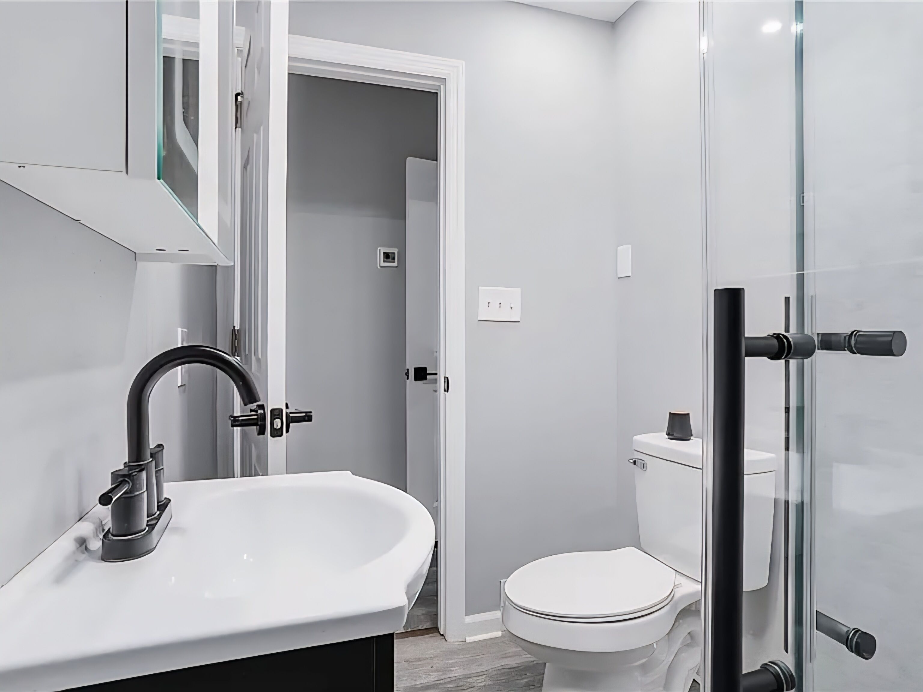 A modern bathroom with a white sink, a toilet, and a glass shower enclosure.