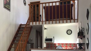Cozinha com escada de madeira, micro-ondas, relógio e painel de azulejos vermelhos e brancos.