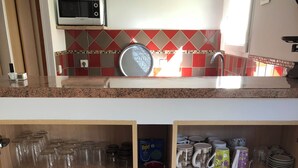 Uma cozinha com micro-ondas, painel de azulejos e prateleiras com pratos, copos e potes.