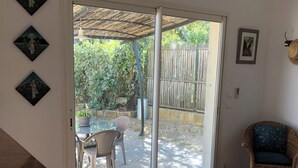 Quarto com porta de correr de vidro para um pátio, uma cadeira de vime, uma mesa pequena e um quadro na parede.