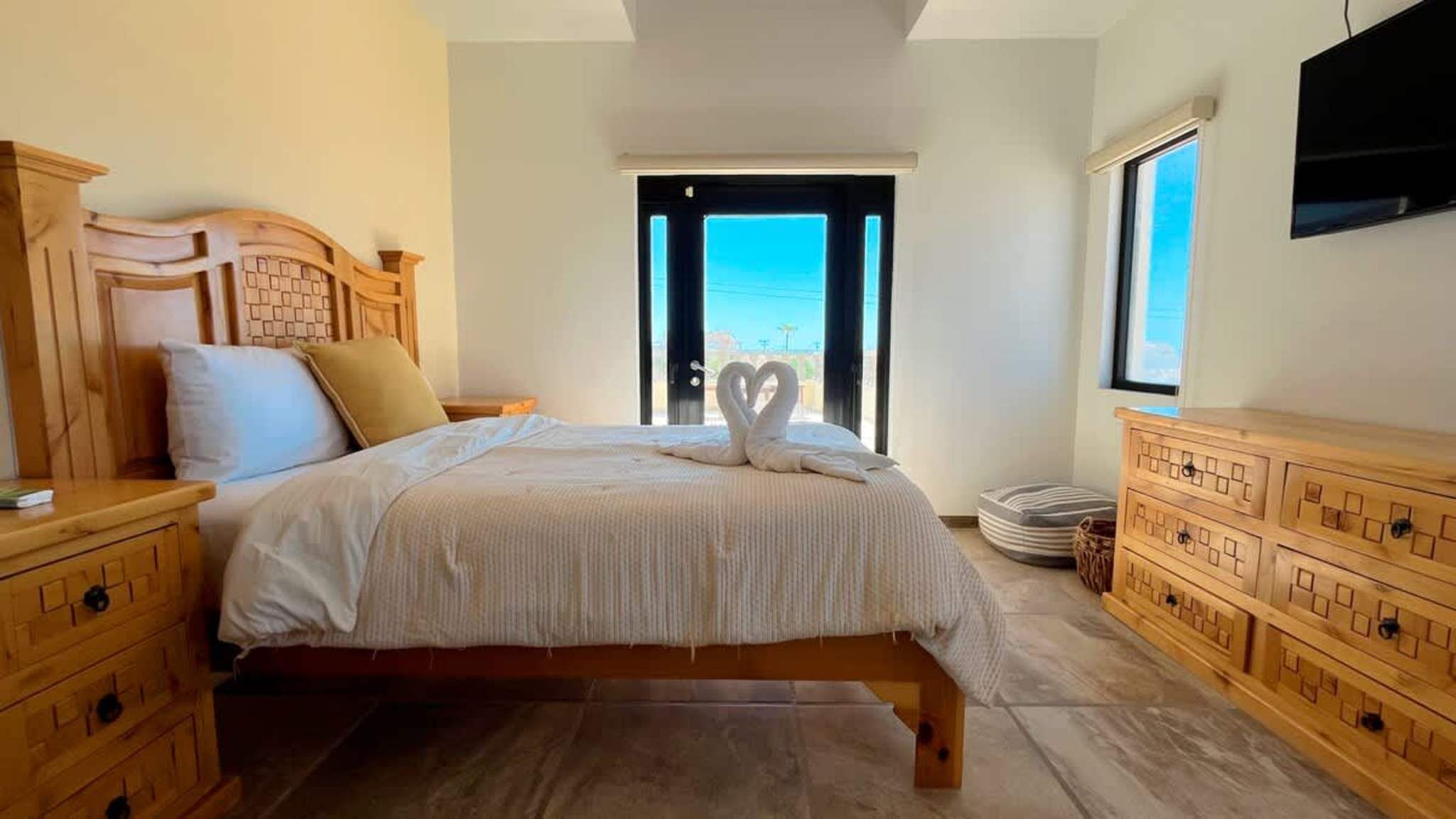 A bedroom with a bed, wooden headboard, bedside tables, a dresser, and a TV.