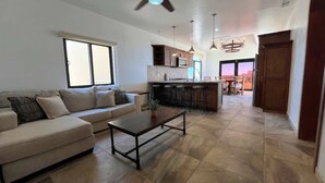 A living room with a sofa, coffee table, and a kitchen area with bar stools.