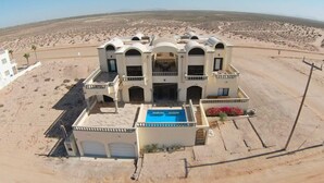 A large, multi-story building with a swimming pool, surrounded by a desert landscape.