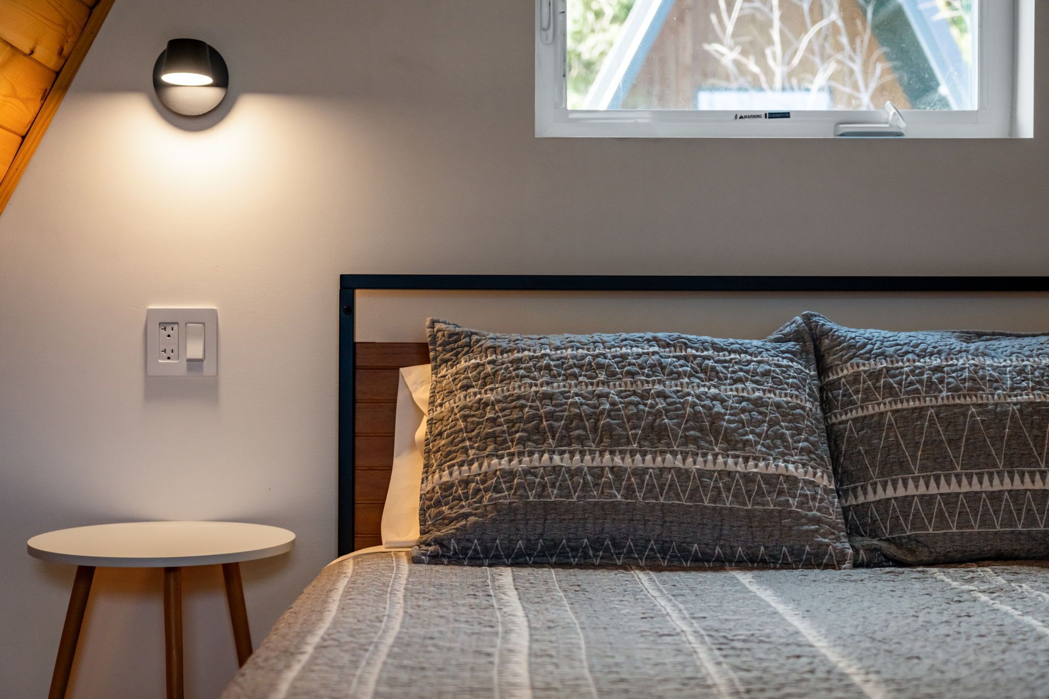 Une chambre à coucher avec un lit, une table ronde, une prise de courant et une fenêtre.