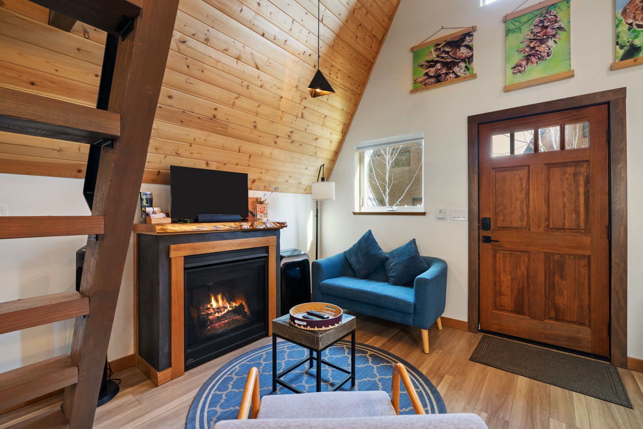 A cozy living room with a fireplace, a blue sofa, a television, and wooden ceiling beams.