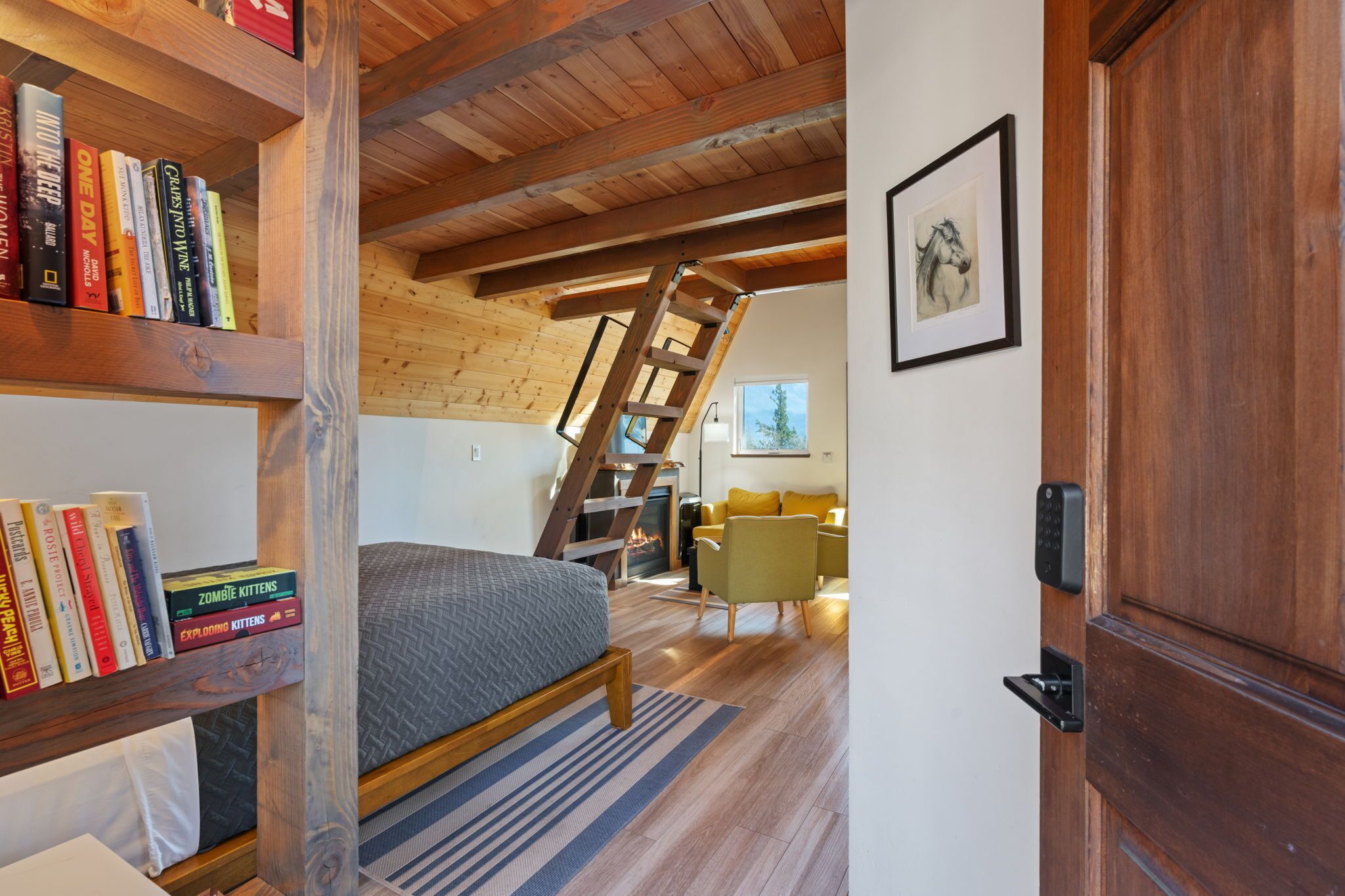 A bedroom with a loft area, a wooden ladder, a bookshelf, a bed, a chair, and a door with a keypad lock.