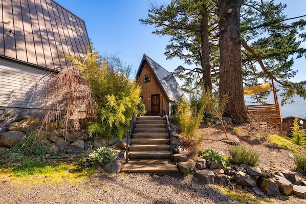 A cabin with a wooden exterior, a stone staircase leading to the entrance, and a large tree to the right. - Artbliss (Stevenson)