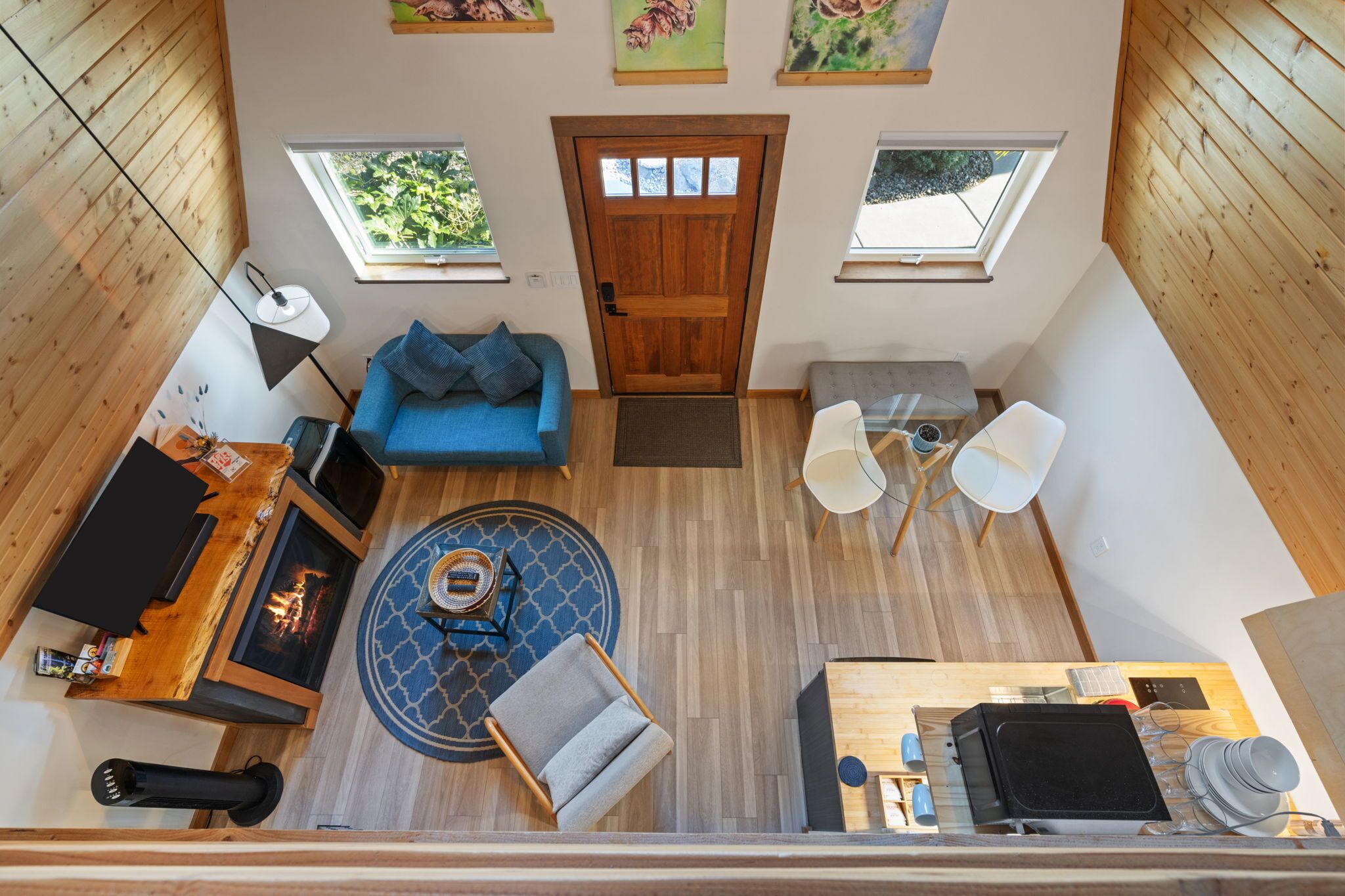 Un intérieur moderne avec un plancher en bois, un canapé bleu, une chaise blanche, une petite table, une cheminée et deux fenêtres.