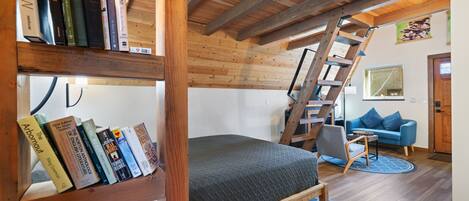 A loft-style room with a bunk bed, a bookshelf, a ladder, a blue couch, and a wooden ceiling.