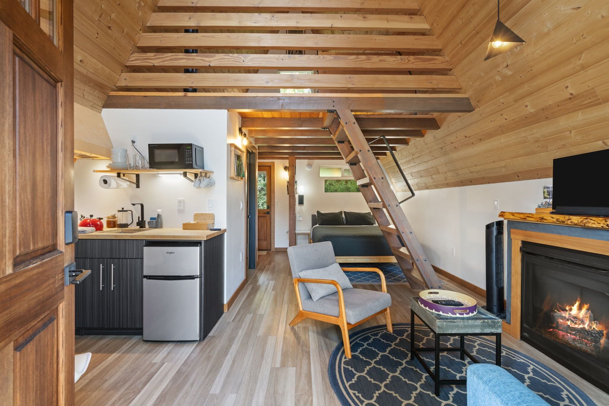 A compact living space with a kitchen, a dining area, a fireplace, and a staircase leading to an upper level.