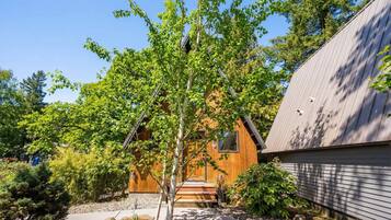 A wooden house with a sloped roof, a small porch, and a garden with various plants and trees.