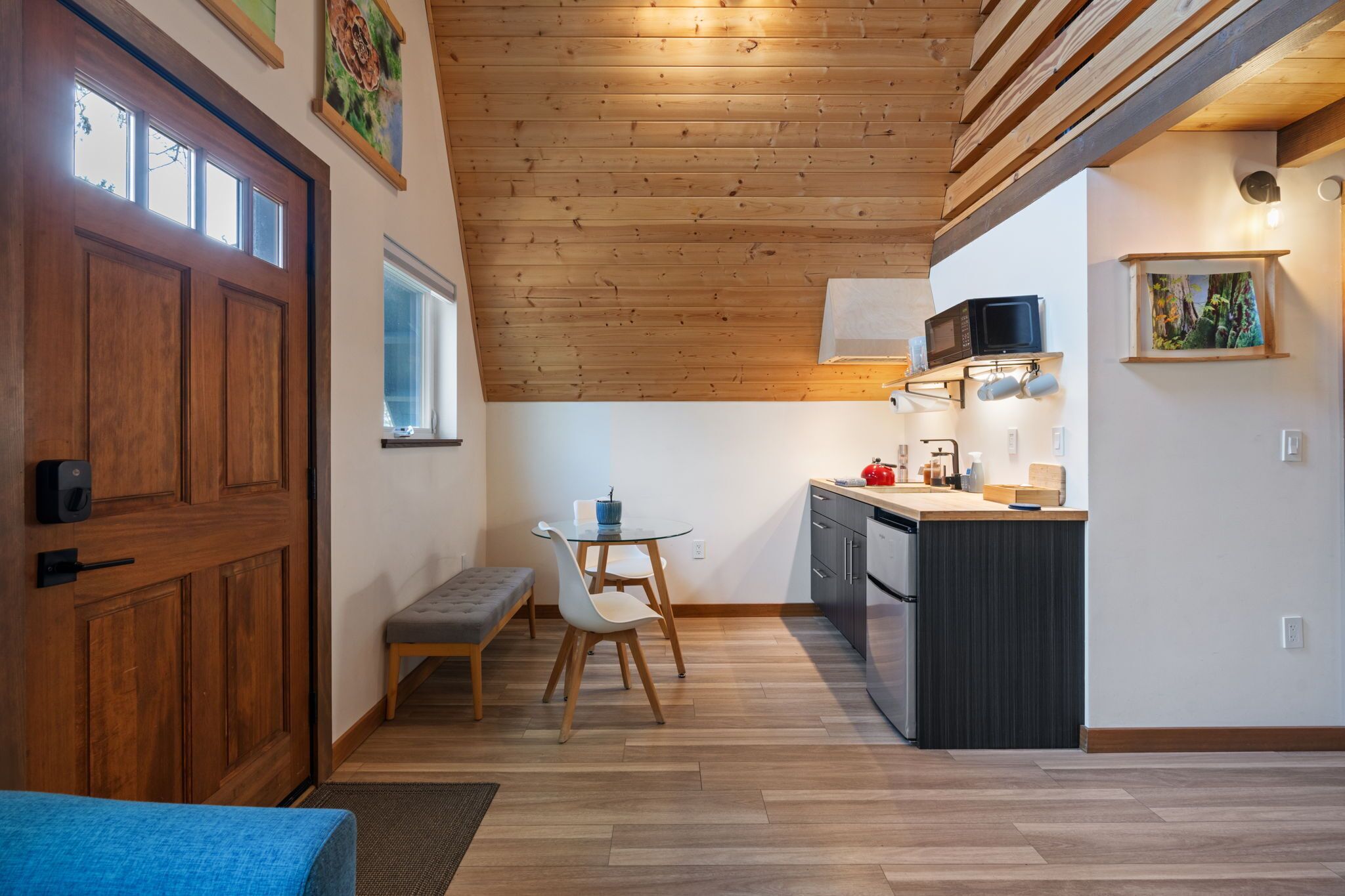 Een moderne keuken met houten vloeren, een eethoek met een bank, een magnetron en een klein schiereiland met een spoelbak.