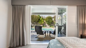 A bedroom with a sliding glass door leading to an outdoor area with a pool, chairs, and a table. - The Cabana Oasis, TOP NOTCH (WOORIM)