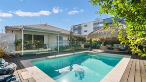 A swimming pool with a wooden deck, a thatched roof structure, and a modern building with large windows. - The Cabana Oasis, TOP NOTCH (WOORIM)