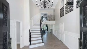 A grand staircase with a chandelier, white walls, and black railings.