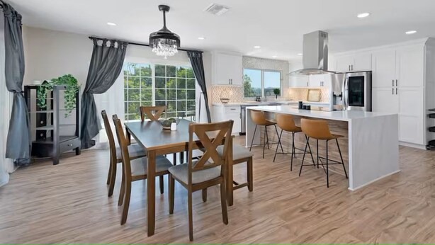 A modern kitchen with white cabinets, a central island, and a dining area with wooden chairs.