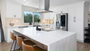 A modern kitchen with white cabinetry, a large island, stainless steel appliances, and a view of greenery outside.