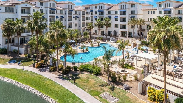 A resort with a central pool, multiple balconies, and palm trees. - The Cays at Ocotillo | Luxury Condo | Resort Pool (Chandler)
