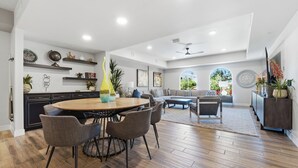 A spacious living area with a dining table, sofas, and a kitchen area with dark cabinetry and decorative items. - The Cays at Ocotillo | Luxury Condo | Resort Pool (Chandler)