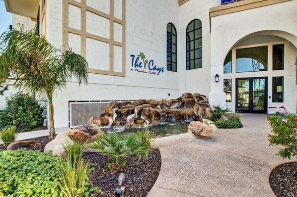 A building with a sign reading 'The Cays' and a water feature with rocks and plants. - The Cays at Ocotillo | Luxury Condo | Resort Pool (Chandler)