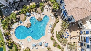An aerial view of a resort with a central swimming pool shaped like a guitar, surrounded by lounge areas, palm trees, and a beach. - The Cays at Ocotillo | Luxury Condo | Resort Pool (Chandler)
