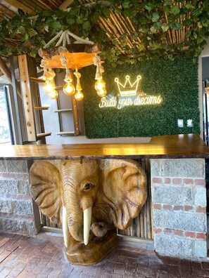 A reception desk with a neon sign, an elephant head sculpture, and a green wall with foliage.