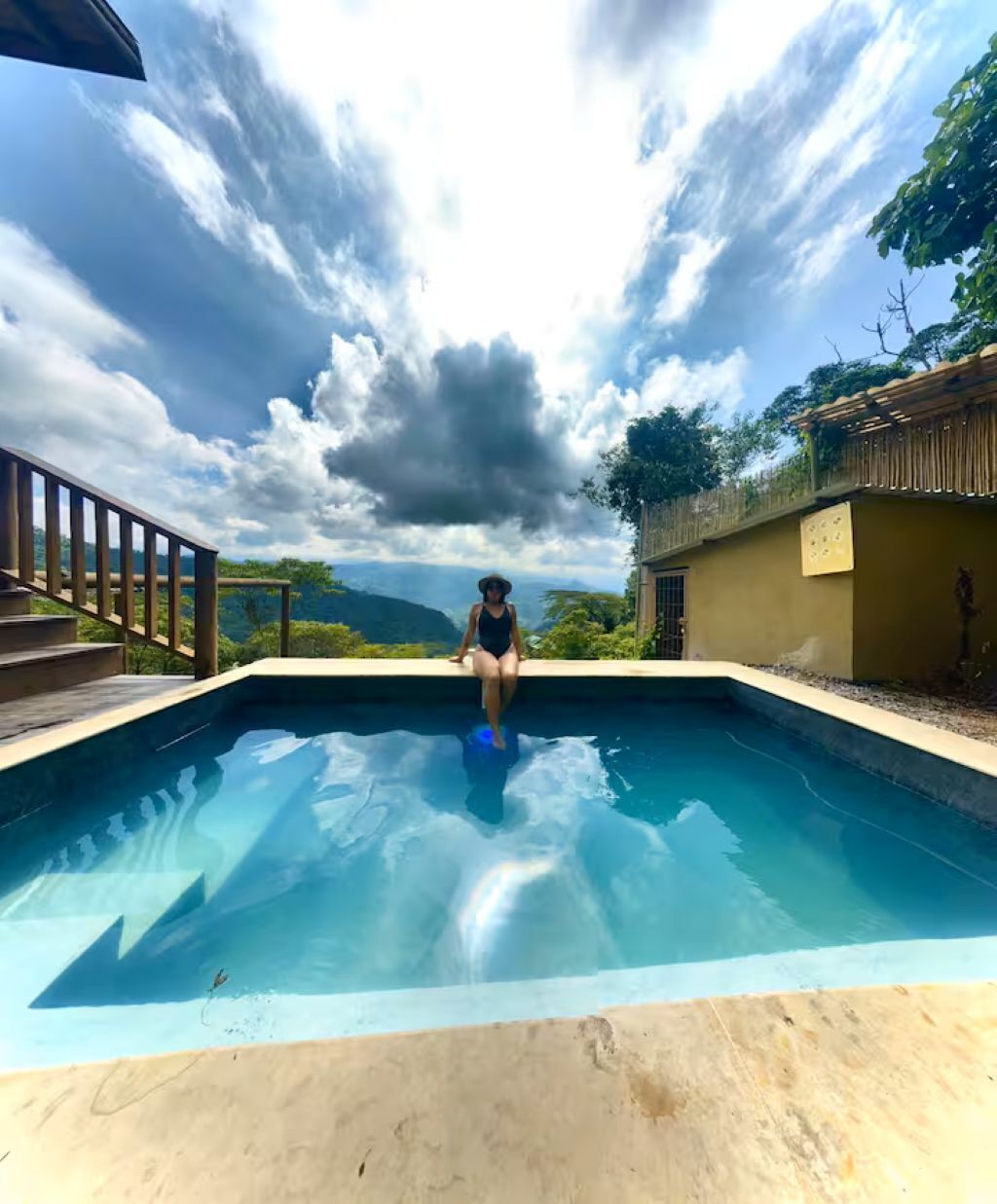 A person sitting at the edge of a pool with a view of mountains and a cloudy sky.