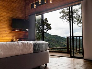 Ein Schlafzimmer mit Bett, Fernseher und einem Balkon mit Bergblick.