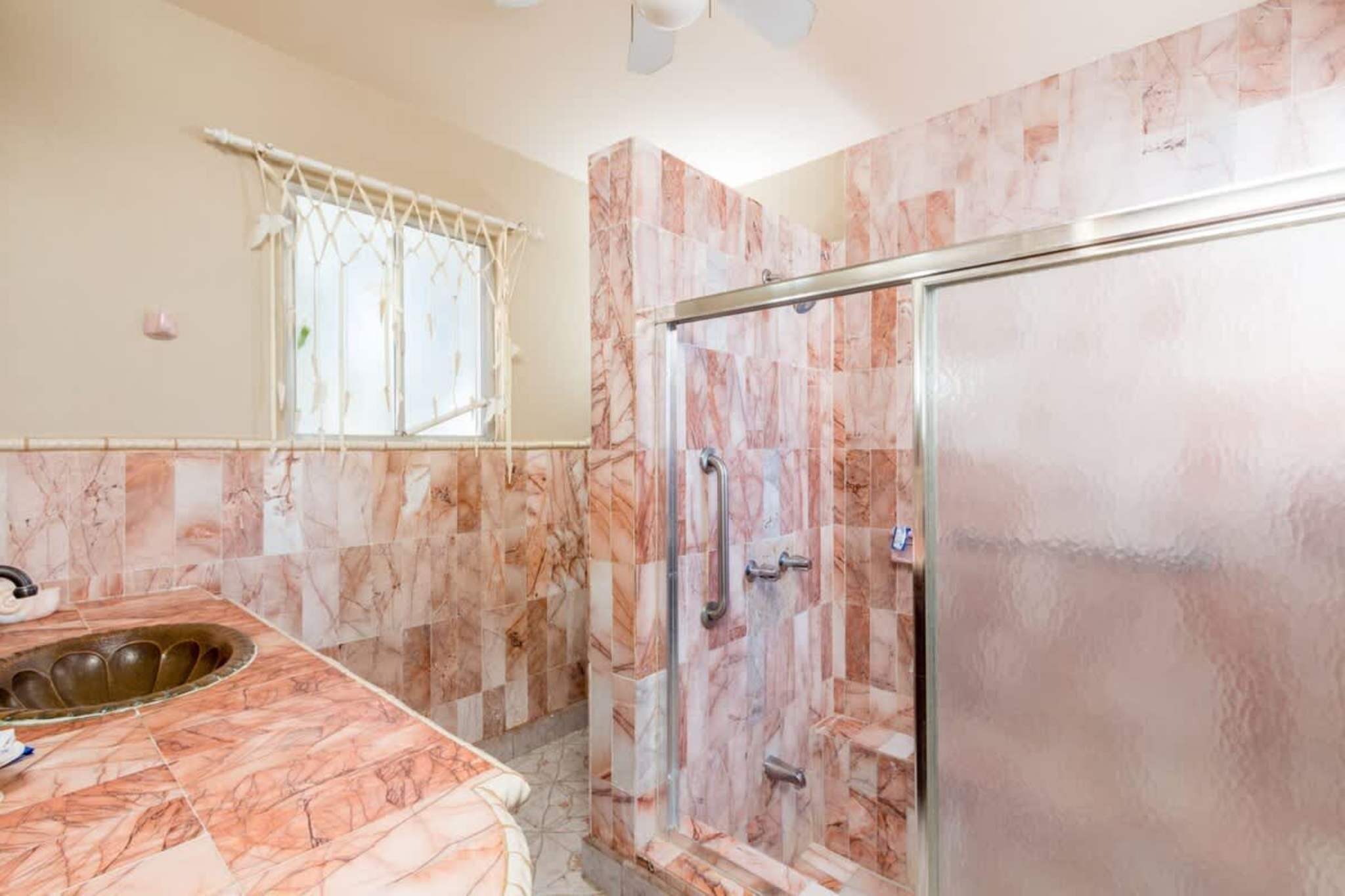 A bathroom with a marble floor, a sink, a shower with a glass door, and a window with a curtain.