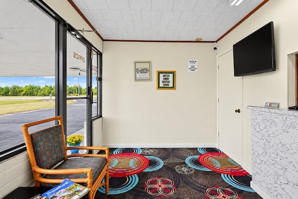 Un área de recepción con una silla, un escritorio, un televisor y una alfombra estampada.