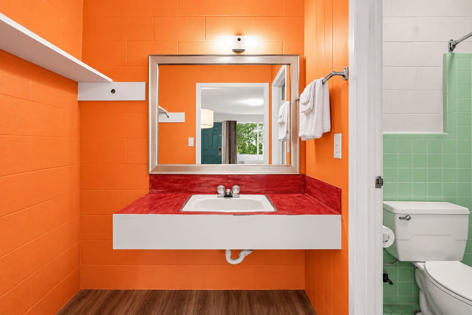 Un baño con una pared naranja, un lavamanos blanco y un inodoro verde.