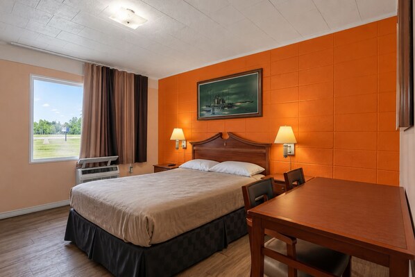A hotel room with a bed, two bedside lamps, a painting on the wall, a window with curtains, and a wooden table.
