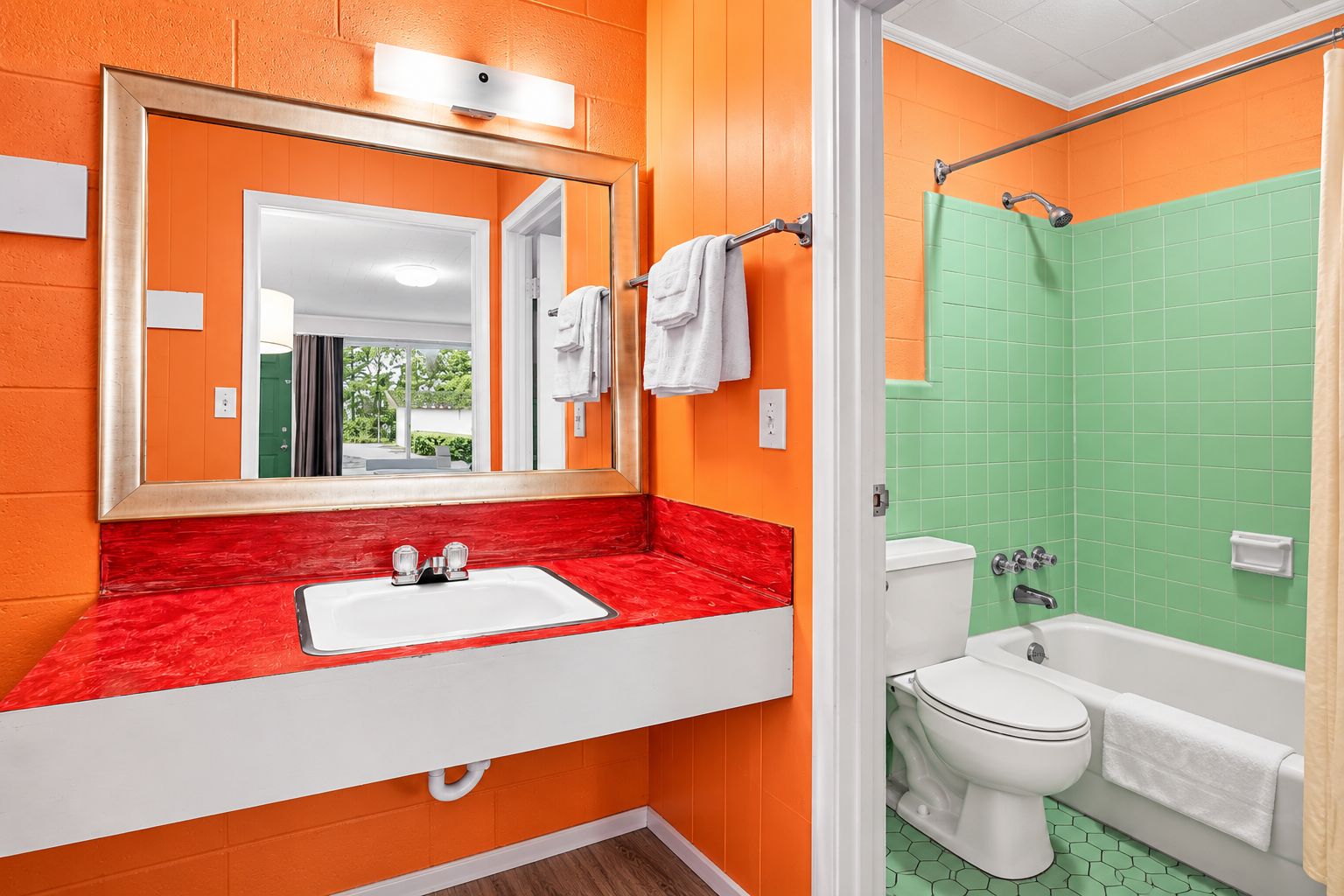Un baño con encimera roja, lavabo blanco y paredes con azulejos verdes.