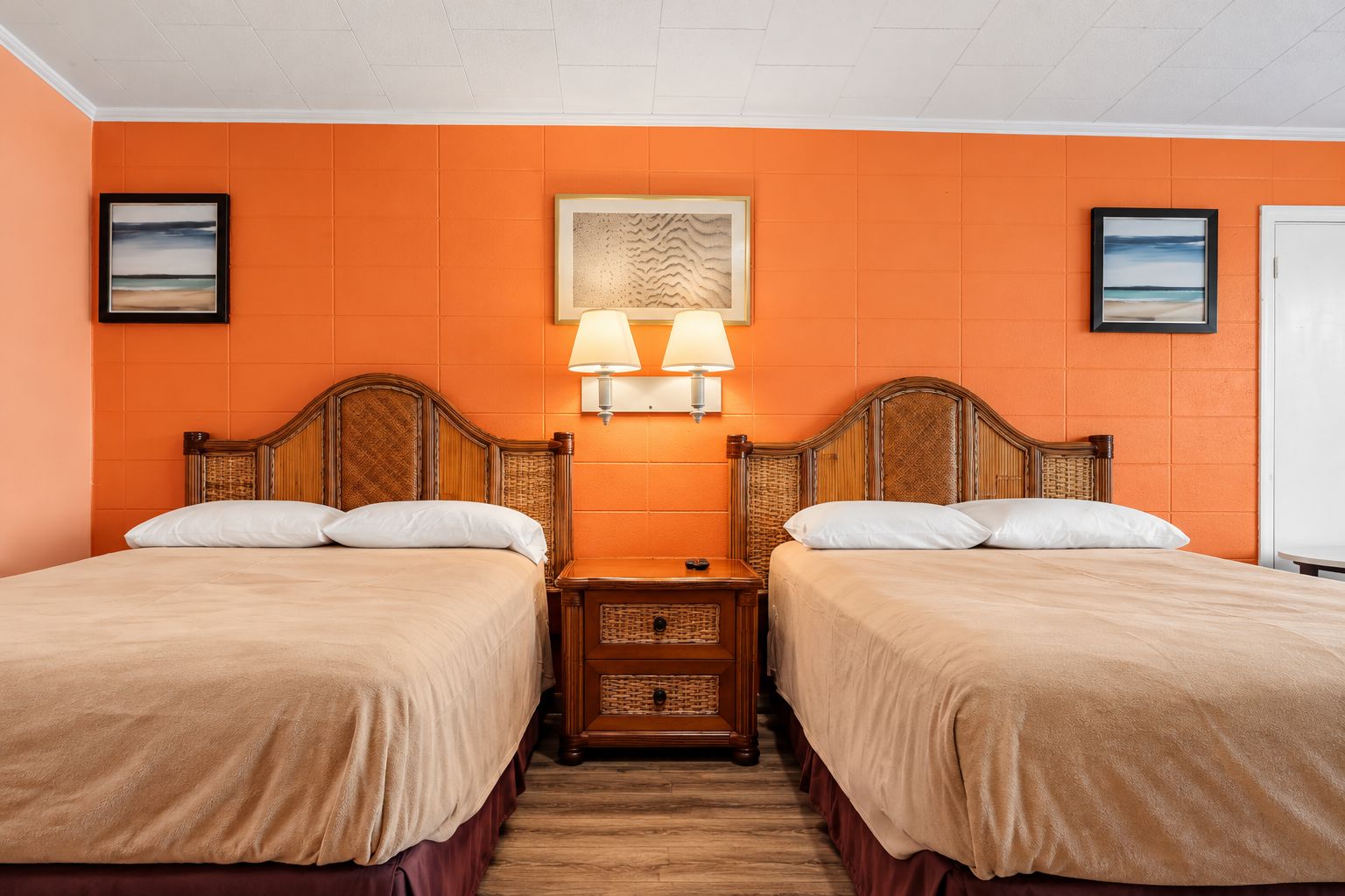 Een hotelkamer met twee bedden, een nachtkastje, een wandlamp en ingelijste foto's.