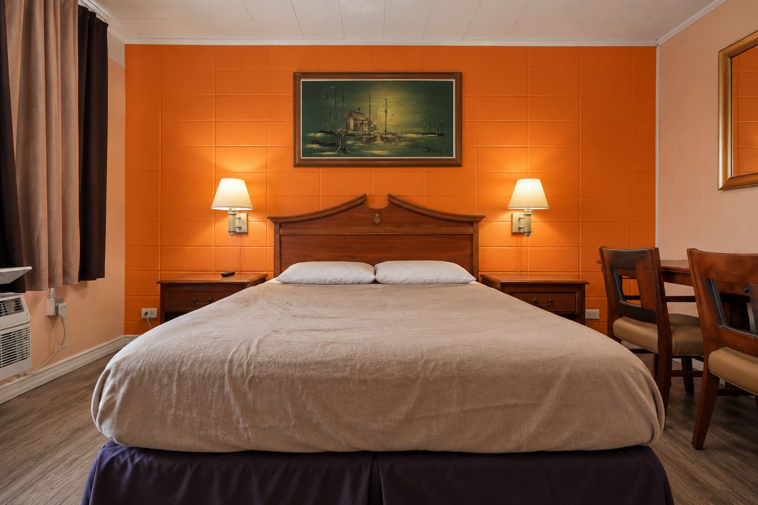 Habitación de hotel con una cama grande, dos mesitas de noche, un escritorio con sillas y un cuadro en la pared.